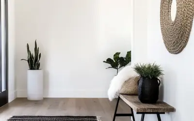 Przytulny przedpokój w stylu boho z drewnianą ławką, plecionym lustrem i roślinami.
