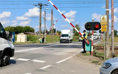 Pracownik obsługuje przejazd kolejowy z zaporami. Czerwone światło sygnalizatora i opuszczone bariery zatrzymują ruch pojazdów.