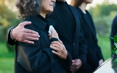 Odprawa pośmiertna: bliscy w żałobie, objęci ramieniem, trzymają chusteczkę.