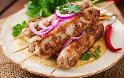 Aksamitny kebab z indyka na talerzu, ozdobiony krążkami czerwonej cebuli i świeżą natką pietruszki. Obok leży pikantna papryczka chili.