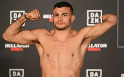 Fighter with one arm boxing, flexing his bicep. He stands against a backdrop of DAZN and Bellator MMA logos.