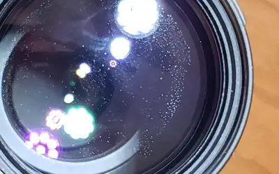 Widoczne na soczewce drobne kropki i kolorowe refleksy, przypominające aberrację chromatyczną, tworzą na czarnym tle ciekawe wzory.