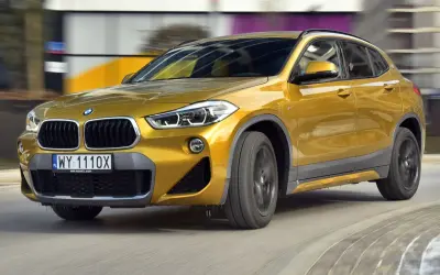 Złoty BMW F39 w ruchu, z widocznym grillem i reflektorami.