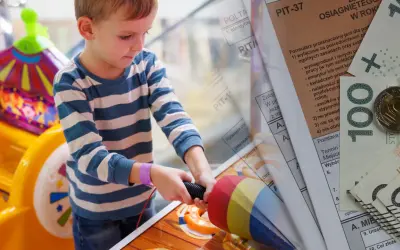 Chłopiec bawi się zabawką, podczas gdy na pierwszym planie widać dokumenty PIT i pieniądze, symbolizujące zwrot podatku na dziecko.