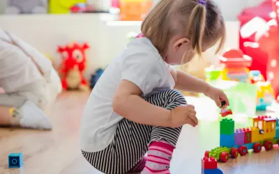 Niña de 0-3 años jugando con bloques de construcción. Crea un tren de juguete y una figura humana.