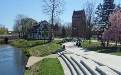 Słupsk atrakcje na weekend: nad rzeką widać zabytkową kamienicę i basztę, spacerują ludzie, kwitną drzewa.