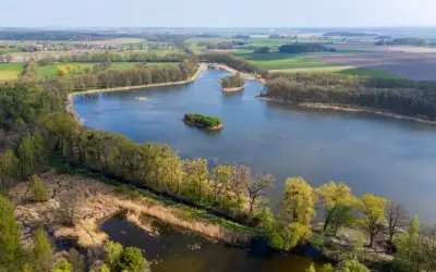 Malownicze jezioro z wyspami, otoczone lasami i polami. Idealne miejsce na romantyczne wypady w Polsce, gdzie można podziwiać przyrodę.