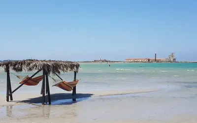 Amache colorate sotto un tetto di paglia, con il mare turchese e antichi edifici all'orizzonte. Un angolo di paradiso a San Teodoro, spiaggia rosa.
