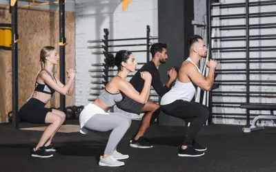 Uomini e donne eseguono squat a corpo libero in palestra, concentrati sull'esercizio.