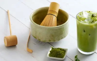 Akcesoria do przygotowania matcha: bambusowa miotełka, miarka, miseczka z proszkiem i szklanka z zielonym napojem. Idealny przepis na matche.