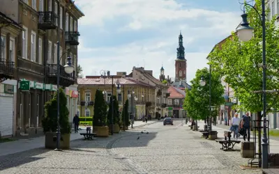Ulica w Radomiu z kamienicami, wieżą kościelną i zielenią.