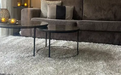 Gemütliches Wohnzimmer mit einem Sofa in greige Farbe, zwei Marmor-Couchtischen und einem flauschigen Teppich.