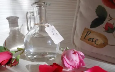Szklana butelka z etykietą "Hydrolat z róży" i płatkami róż. Idealny sposób, jak zrobić hydrolat w domu.