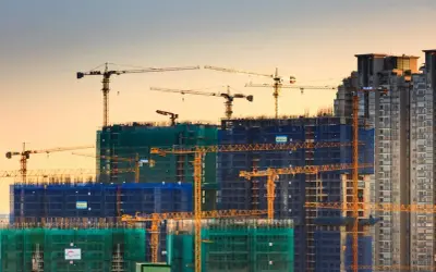 Grúas de construcción trabajando en la edificación de rascacielos, mostrando los elementos estructurales de un edificio en proceso.