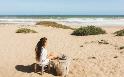 Kobieta pije herbatę na piaszczystych plażach Tunezji, z widokiem na ocean i falujące morze.