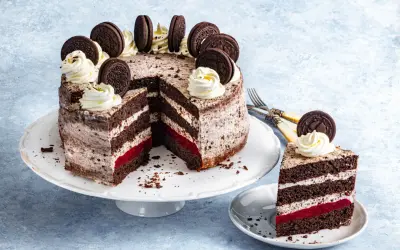 Pyszny tort oreo z kremem, malinową warstwą i ciasteczkami oreo na wierzchu. Kawałek ciasta na talerzyku.