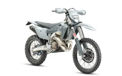 Szary motocykl Husqvarna z oponami terenowymi na białym tle.