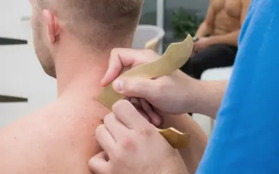 Masaż karku i ramion przy użyciu narzędzi do pinoterapii. Terapeuta wykonuje ruchy narzędziem po skórze pacjenta.