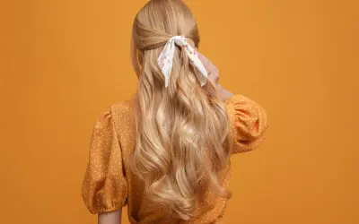 Chevelure blonde ondulée, coiffée en demi-queue avec un foulard fleuri, sur fond orange.