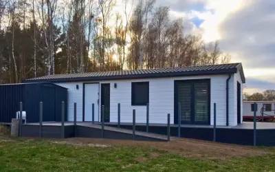 Nowoczesne domki letniskowe przystosowane dla osób niepełnosprawnych, z podjazdem i tarasem, otoczone drzewami.
