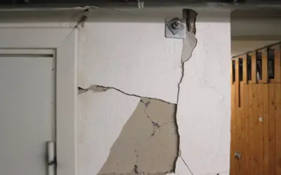 Stora sprickor i väggen visar behovet av att laga sprickor i grunden. En metallplatta med bult sitter fast i den spruckna väggen.