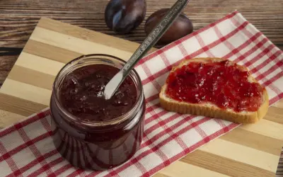 Un pot de confitures de quetsches maison, une tartine généreusement garnie et quelques quetsches sur une planche en bois.