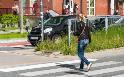 Młoda kobieta, pieszy, idzie przez pasy, patrząc w telefon.