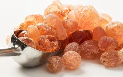 Grains ambrés de gomme arabique dans une cuillère métallique. Qu'est-ce que la gomme arabique ? Une résine naturelle aux multiples usages.