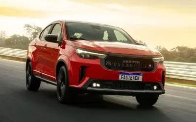 La Fiat Fastback 2026 rossa sfreccia su una pista, con il sole che illumina il cielo.