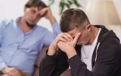 Zmartwiona kobieta siedzi obok męża, który opiera głowę na dłoniach. Podejrzewam, że mąż bierze narkotyki.