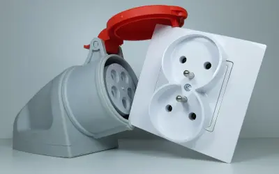 Szara wtyczka przemysłowa i biała podwójna gniazdko elektryczne. Zastanawiasz się, ile kosztuje założenie siły w domu?