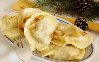 Pyszne pierogi z mięsem i kapustą, okraszone skwarkami, na talerzu z gałązką sosny i szyszkami.