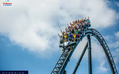 Ludzie krzyczą z radości na pokładzie Hyperiona, największego rollercoastera w Polsce, pędząc po stalowych torach na tle błękitnego nieba.