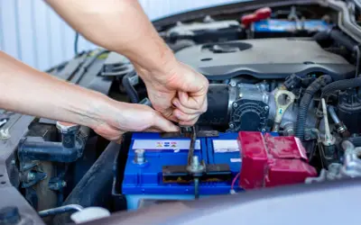 Ręce mechanika dokręcają klemę akumulatora. Widać silnik i elementy instalacji elektrycznej, czuć napięcie przed uruchomieniem.