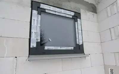 Nowe okno w szarej ramie, otoczone taśmą montażową. Rozważasz wymiana okien cena? To dobry moment na inwestycję.