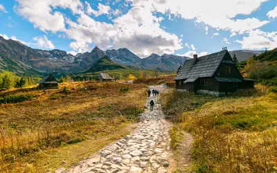 Kamienna ścieżka prowadzi do górskich chat. W oddali majestatyczne Tatry. To piękne zakopane atrakcje.