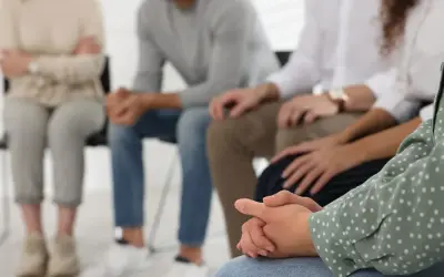 Grupa osób siedzi w kręgu, wspierając się nawzajem. To obraz nadziei i wspólnej drogi w terapii od uzależnień.