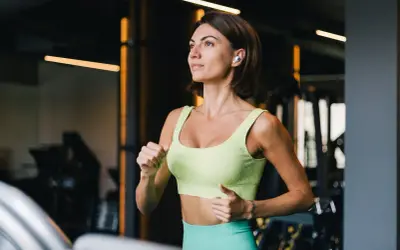 Kobieta w sportowym stroju biegnie na bieżni w siłowni.