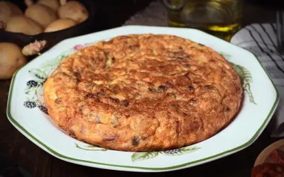 Tortilla española, un clásico de la comida típica de Granada, servida en un plato decorado. Patatas y aceite en el fondo.