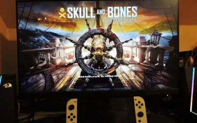 Logo gry "Skull and Bones" z kołem sterowym ozdobionym czaszką i kośćmi.