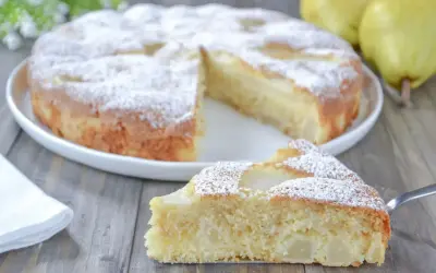 Una fetta di torta pere soffice e profumata, cosparsa di zucchero a velo, su un tavolo di legno.