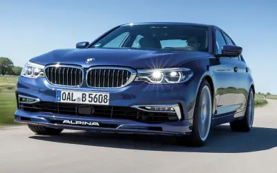 Niebieskie BMW Alpina pędzi po krętej drodze, błyszcząc w słońcu.