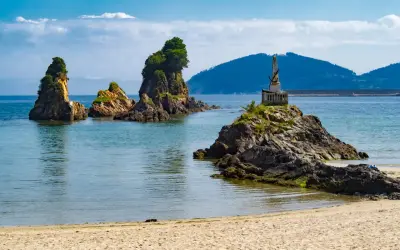 Rocas emergiendo del mar azul, un monumento en una de ellas, y la arena dorada de las playas cerca de Viveiro.