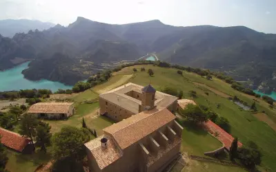 Edificio histórico en la Serra de Busa, con un lago turquesa y montañas al fondo.