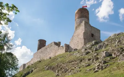 Ruiny zamku na skalistym wzgórzu w paśmie gór świętokrzyskich. Biało-czerwona flaga powiewa na wieży.