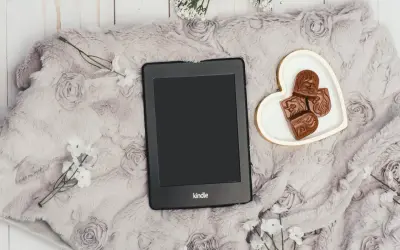 Elegancki Kindle na miękkim kocu z różami, obok serduszka z czekoladkami. Idealny zestaw, by dowiedzieć się, jak pobierać książki na Kindle.