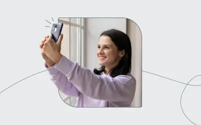 Uśmiechnięta dziewczyna robi selfie telefonem, jakby korzystała z automatu do robienia zdjęć do dowodu.