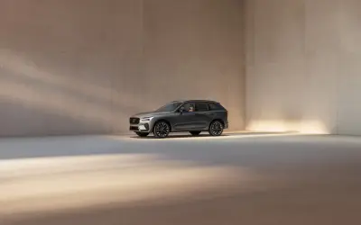 En mörkgrå Volvo XC60 står i ett ljust, minimalistiskt rum. Bilen visar upp sina eleganta linjer och fälgar, en perfekt representation av Volvo utrustningsnivåer.