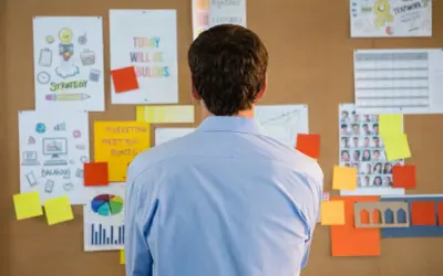 Uomo osserva bacheca con grafici, foto e note. I turni di lavoro devono essere esposti chiaramente per tutti.