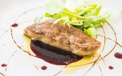 Un morceau de foie gras poêlé, servi avec une sauce aux fruits rouges et une salade verte. Une recette raffinée pour un plat d'exception.